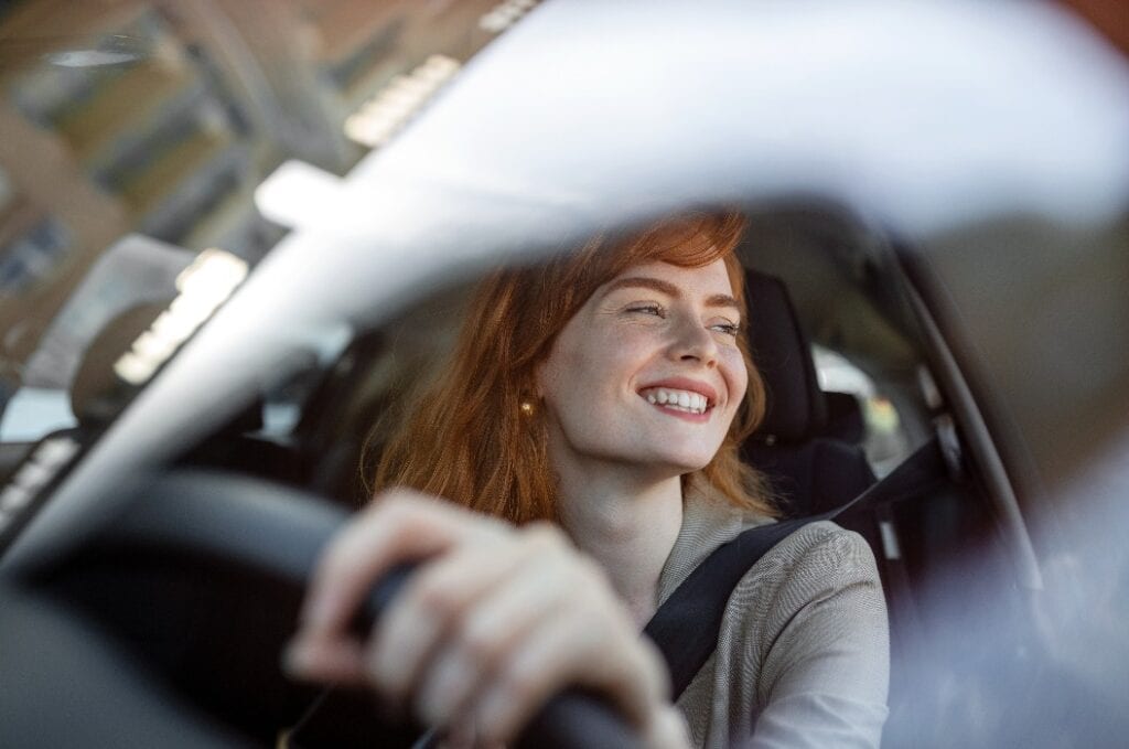 Beautiful young woman driving her new car at sunset. Woman in car. Close up portrait of pleasant looking female with glad positive expression, woman in casual wear driving a car