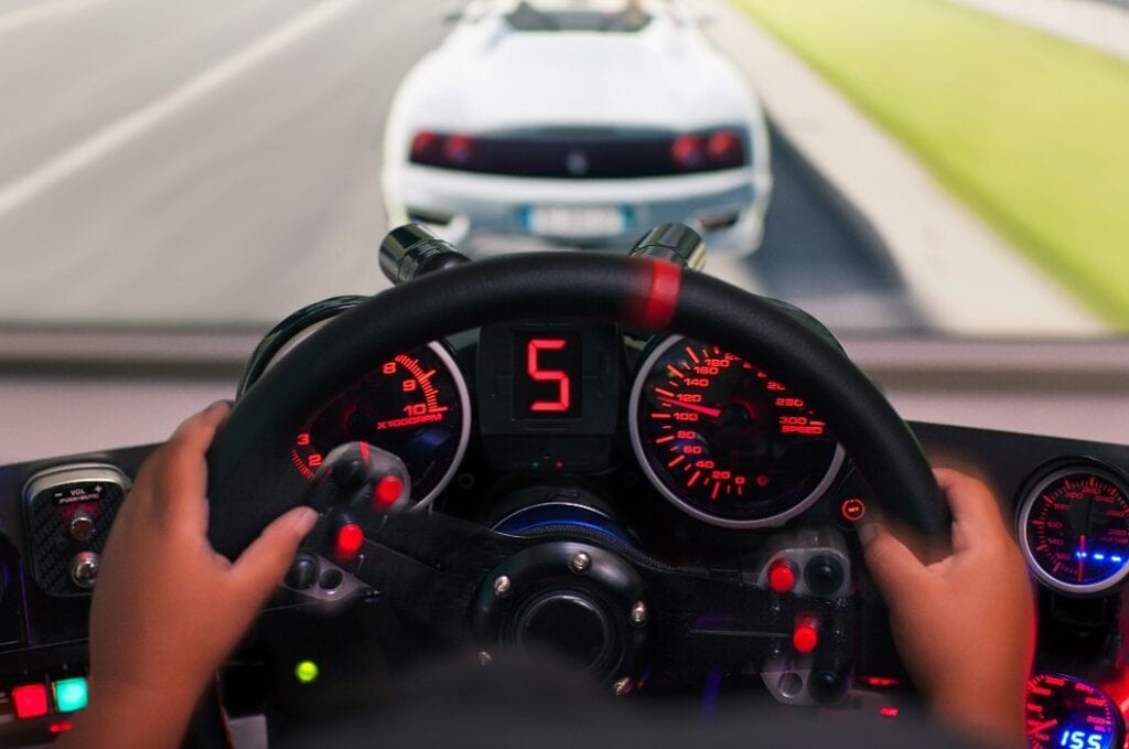 Hands of a kid on a steering wheel, while he plays a racing game in a realistic looking racing seat with gauges.